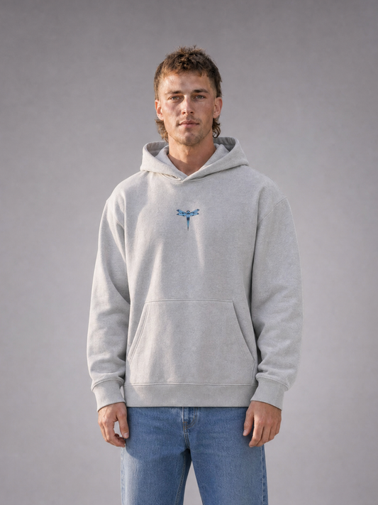 TRUST THE CHAOS Heavy Hoodie grey - Frontansicht, getragen von männlichem Model, mit kleinem blauen Libellen-Logo auf der Brust [KI]