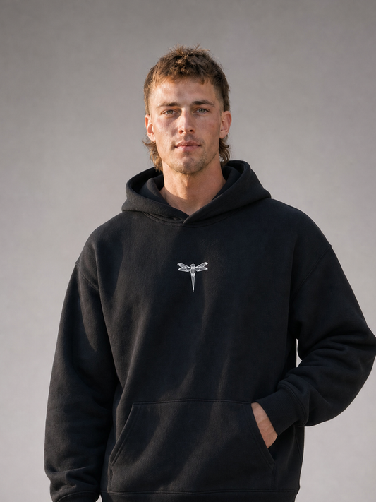 TRUST THE CHAOS Hoodie black – Frontansicht, getragen von männlichem Model, mit gesticktem Libellen-Logo auf der Brust [KI]