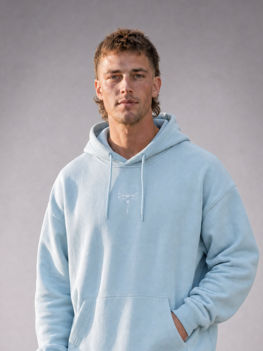 TRUST THE CHAOS Hoodie blue - Nahaufnahme Frontansicht, getragen von männlichem Model, mit kleinem weißen Libellen-Logo auf der Brust [KI]